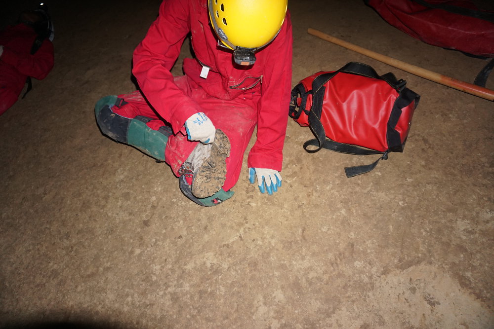 A caver cleaning mud out of his shoe tread.